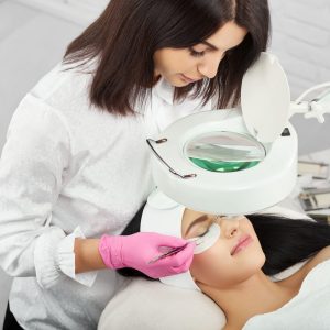 Professional lashmaker working with a client in beaty salon. Woman lying on cosmetologiacal coach during lashes enlarging. woman with pretty face wearing headbandage and stickers for lashmaking .