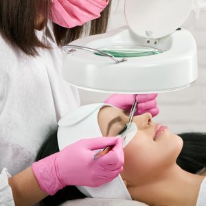Professional working with a client in beaty salon. Woman lying on cosmetologiacal coach during lashes enlarging. Model with pretty face wearing headbandage and stickers for lashmaking .