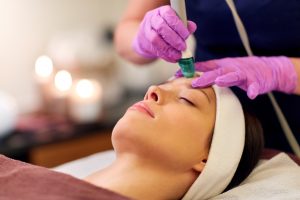 people, beauty, cosmetology, exfoliation and technology concept - beautiful young woman having microdermabrasion facial treatment with crystals in spa