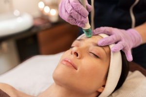 people, beauty, cosmetology, exfoliation and technology concept - beautiful young woman having microdermabrasion facial treatment with crystals in spa